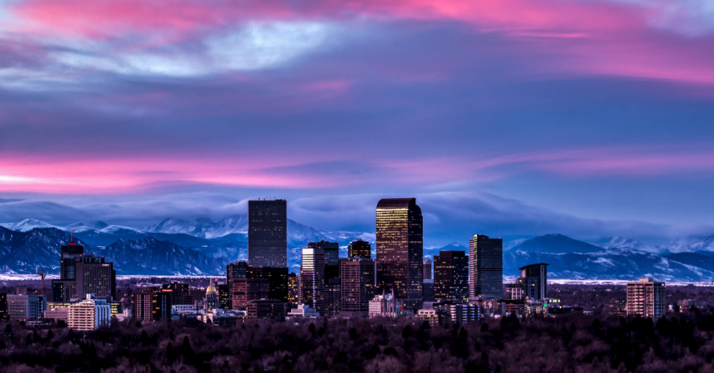 Denver skyline at dusk with the Rocky Mountains behind it under a pink-purple sky, echoing the Gartner Supply Chain Planning Summit in Denver.